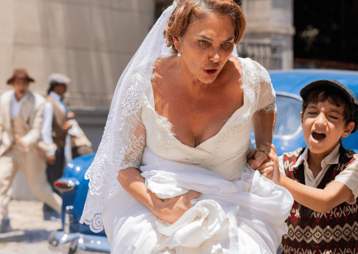 Zulma (Heloisa Périssé) impede que Samir (Davi Milazia) seja atropelado pelo bonde após o menino fugir dela e correr para Candinho (Sergio Guizé)